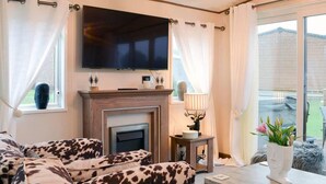 A living room with a sofa set, a fireplace, a television, and a view of the outside. - Boutique Lodge With hot tub Sleeps 6 (Bridlington)