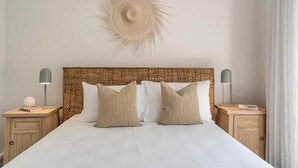 A neatly made bed with a woven headboard, two bedside tables with lamps, and a decorative wall piece. - Getawayz NSW -  'Drift' - Absolute Beachfront at Coledale w/ Panoramic Views & Multiple Living Zones (Coledale)