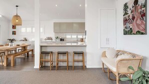 A modern kitchen with white cabinets, a central island, and bar stools. - Getawayz NSW -  'Drift' - Absolute Beachfront at Coledale w/ Panoramic Views & Multiple Living Zones (Coledale)