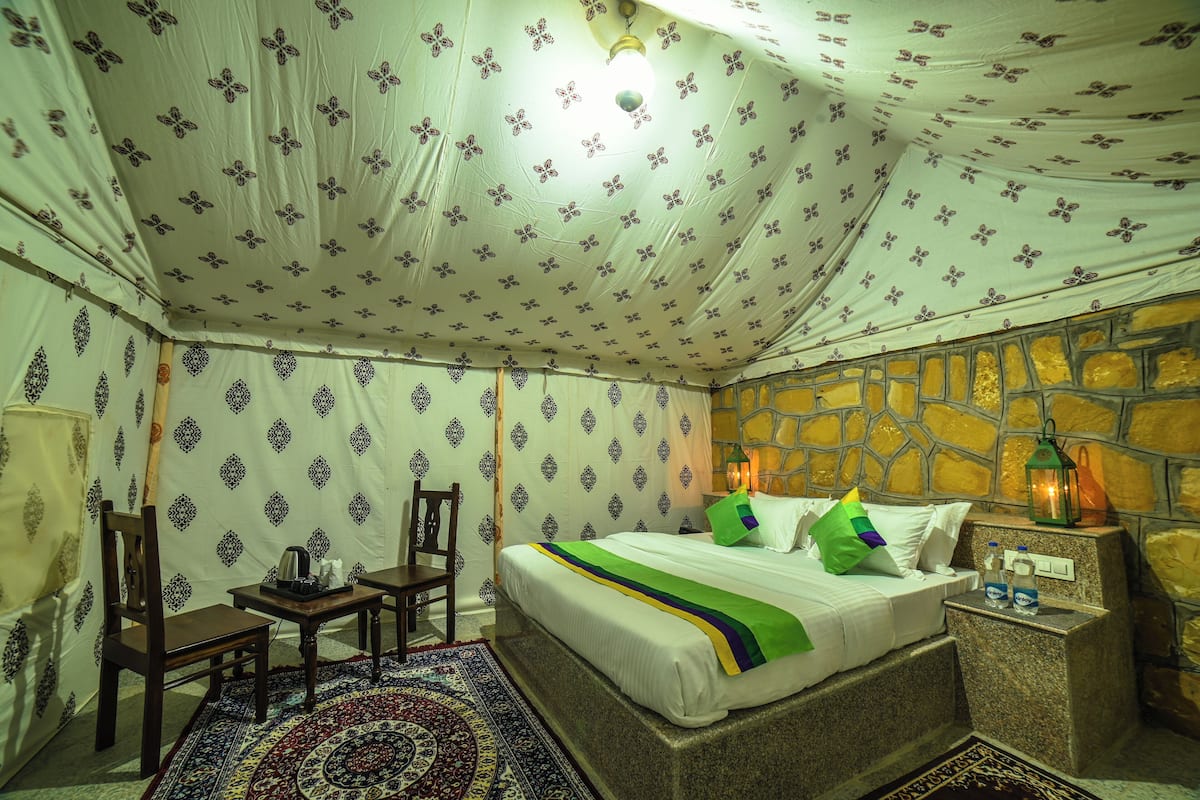 Una habitación con cama, una silla, una mesa, una lámpara y una pared con diseño de piedra.