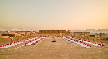 Un resort en el desierto con varias tiendas blancas, filas de sillones y tumbonas dispuestas en una distribución simétrica.