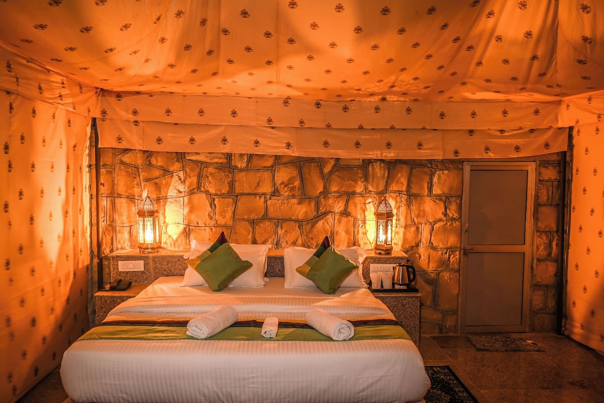 Una habitación con pared de piedra, una cama con almohadas, una mesita de noche con un farol y una puerta.