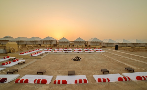 A desert resort with multiple tents and lounge areas with sunbeds and small tables.