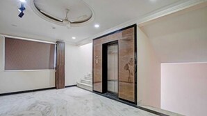 Un vestíbulo amplio con piso de mármol, una pantalla grande montada en la pared y un ascensor con detalles de mármol.