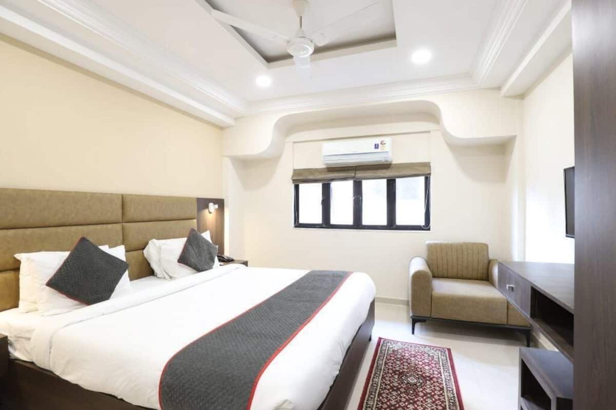 A hotel room with a large bed, a sofa, a TV, and an air conditioning unit.
