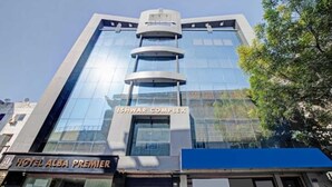 Un moderno edificio de hotel con fachada de vidrio y un cartel que indica "ISHWAR COMPLEX" y "HOTEL ALBA PREMIER" debajo.