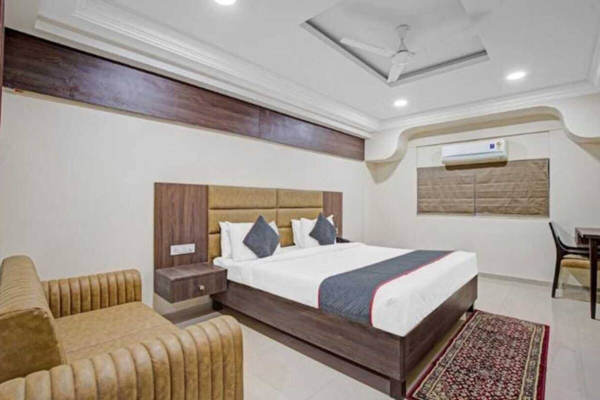 A hotel room with a large bed, a wooden headboard, a small bedside table, a sofa, and a patterned rug.