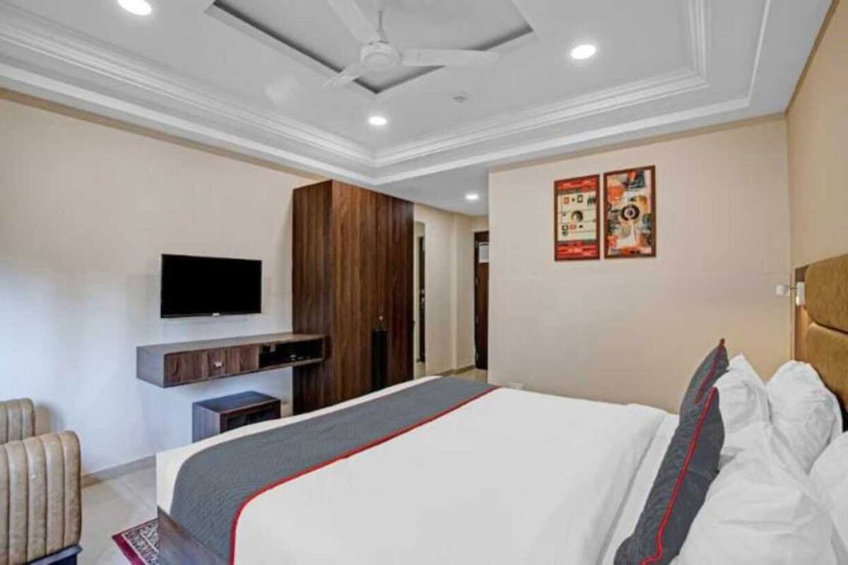 A hotel room with a bed, a television mounted on the wall, a wooden wardrobe, and a red and white bedspread.