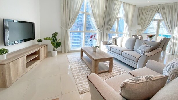 Un salon moderne avec un téléviseur à écran plat, un meuble de rangement en bois, un canapé beige et une table basse.
