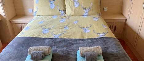 Cama com colcha estampada e travesseiros, duas toalhas dobradas e parede decorada.