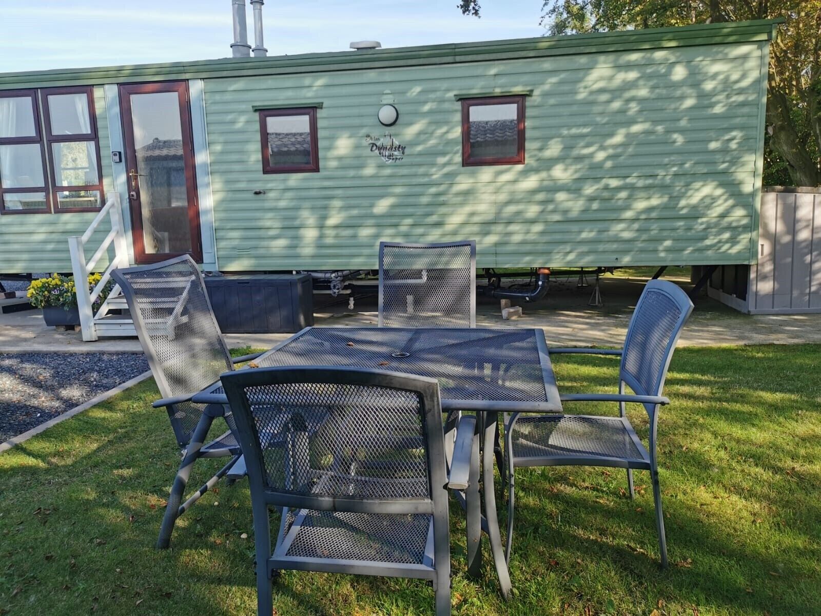 A green mobile home with a patio area featuring metal chairs and a table.