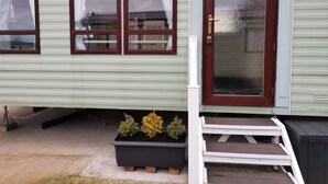 Una casa con puerta principal, tres ventanas, un pequeño porche con escalones y una maceta con plantas.