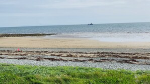 Una playa con costa rocosa y un barco a lo lejos.