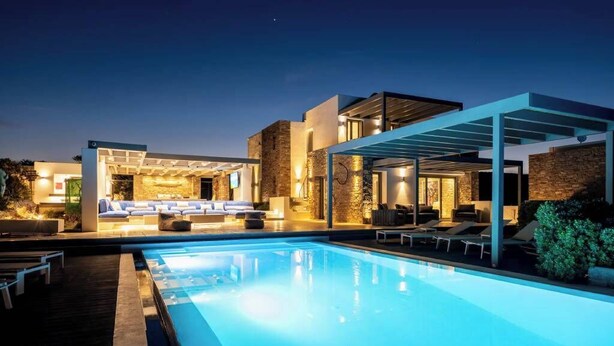 A modern poolside area with a clear pool, lounge chairs, and a covered seating area.
