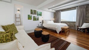 A modern bedroom with a large bed, a sofa, and a view of the outdoors.
