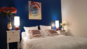 A bedroom with a blue accent wall, a white bed with patterned pillows, bedside tables with lamps, and a painting above the bed.