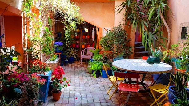 A courtyard with a round table and chairs, surrounded by potted plants and flowers.