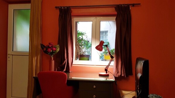 Une pièce comprenant un bureau, une chaise, une lampe et une fenêtre avec des rideaux.