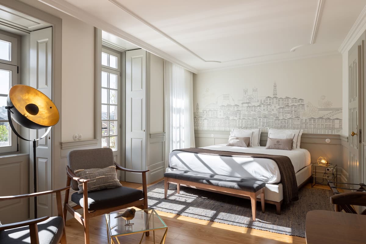 Une chambre avec un lit, une chaise, une table et une fresque murale représentant un paysage urbain.