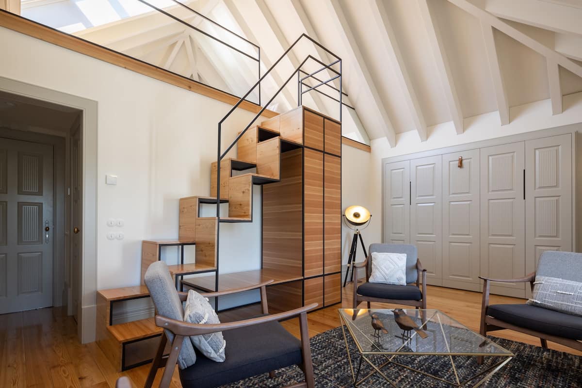 Un salon moderne avec un escalier en bois, une table basse en verre et une vue sur le ciel grâce à un plafond incliné.