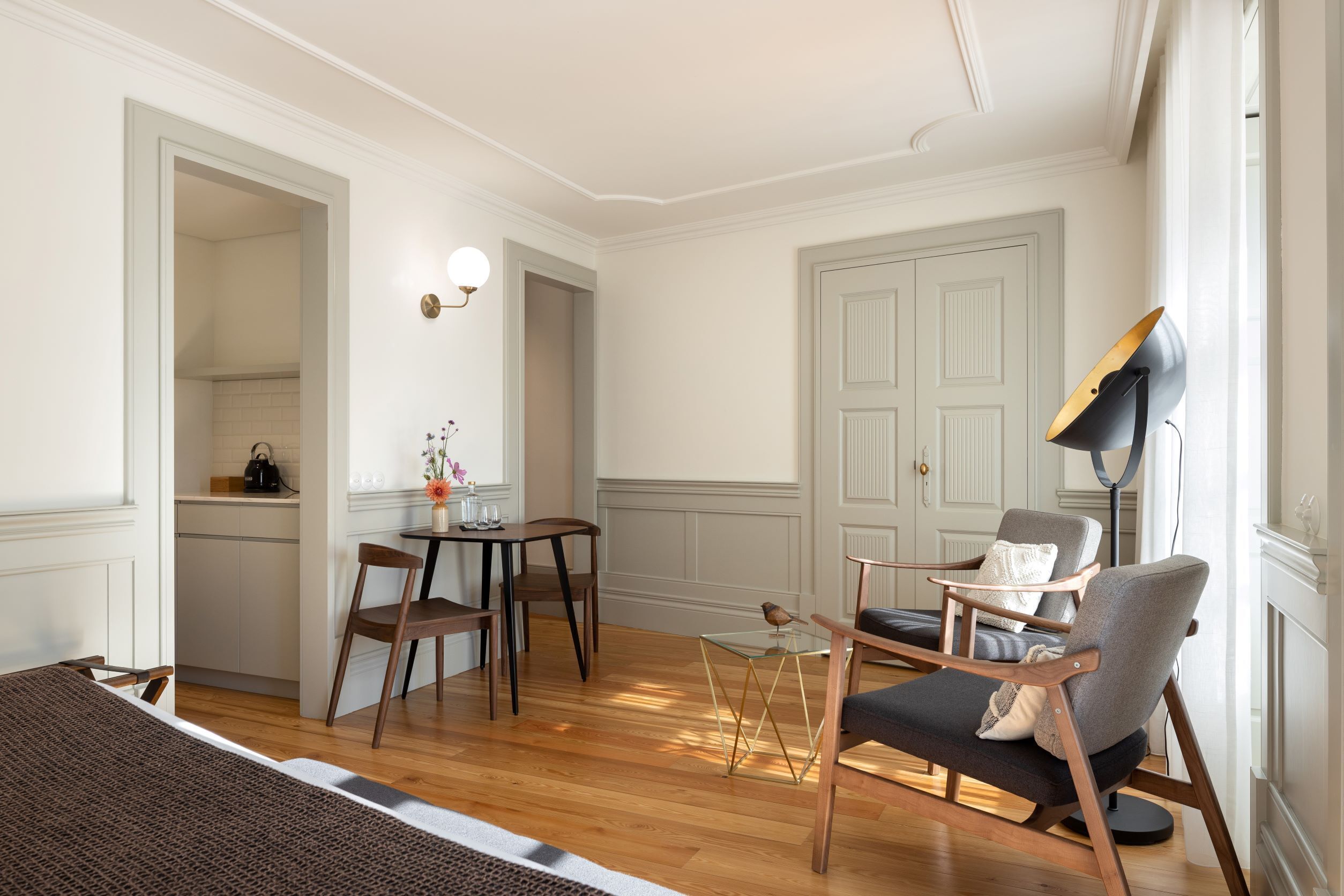 Una habitación luminosa con suelo de madera, una mesa de comedor con sillas, un sofá y una lámpara de pie.