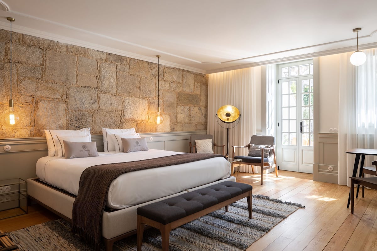 Une chambre avec un grand lit, un banc, une chaise, un bureau et un mur en pierre.