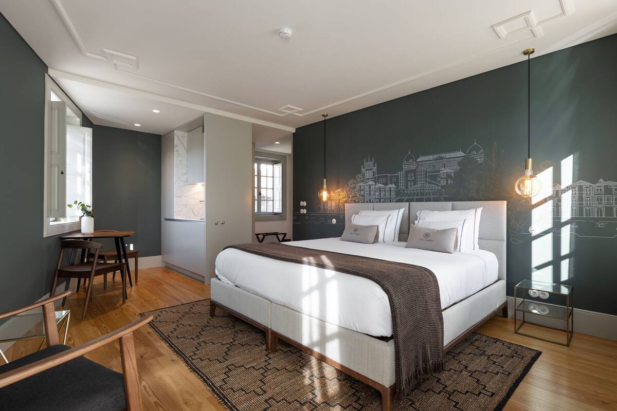 Une chambre moderne avec un grand lit, une fresque représentant un paysage urbain et un coin repas avec une table et des chaises.