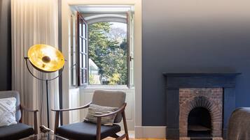 Una habitación con chimenea, una ventana con cortinas, una silla y una lámpara de pie.