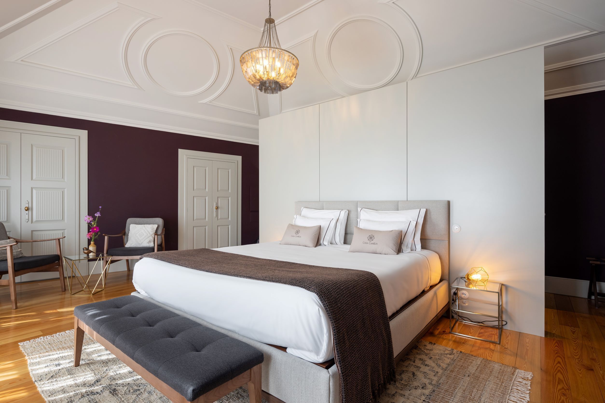 Une chambre à coucher avec un grand lit, un banc, une table de chevet avec une lampe et un lustre.