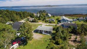 An aerial view of a coastal residential area with houses, a road, and a body of water.