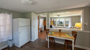 A kitchen with a refrigerator, wooden dining table, chairs, and a window with a view.
