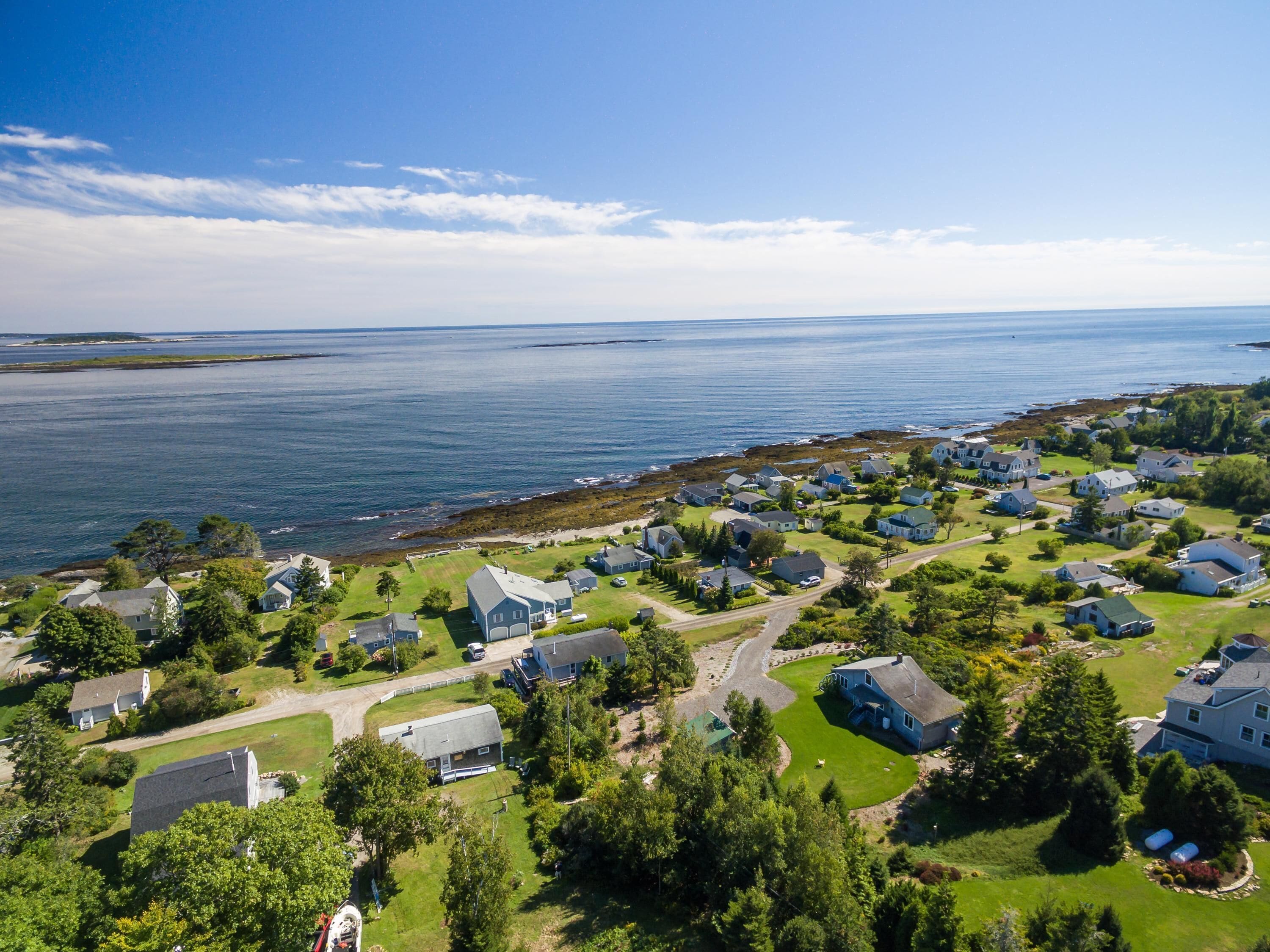 Vue aérienne d’un quartier résidentiel situé sur la côte, avec des maisons, des pelouses verdoyantes et une vue dégagée sur l’océan.