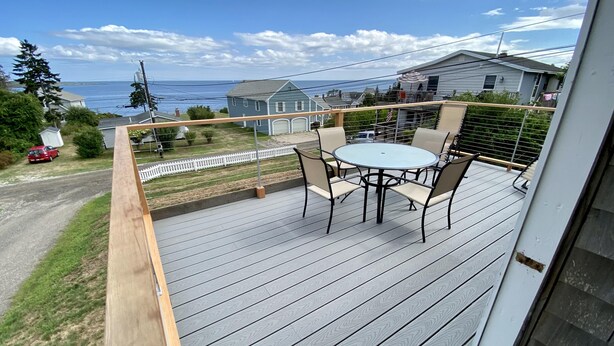 A deck with a table and chairs, overlooking a residential area and the sea.