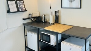 Une cuisine compacte équipée d’un four à micro-ondes, d’un grille-pain et d’un petit réfrigérateur. Un certificat encadré est accroché au mur, ainsi qu’un luminaire décoratif.