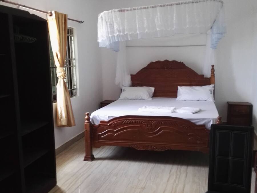 Une chambre avec un lit en bois, un ventilateur de plafond et une chaise noire.