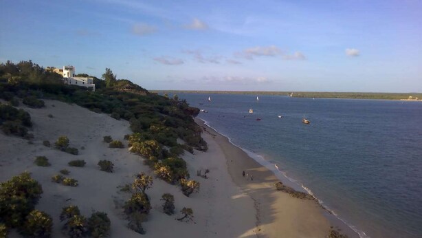A coastal landscape with a sandy beach, sparse vegetation, and a few boats on the water. - Wiyoni Royals Lamu (Lamu)