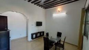 A room with a dining table and chairs, a TV mounted on the wall, and a ceiling fan. - Wiyoni Royals Lamu (Lamu)