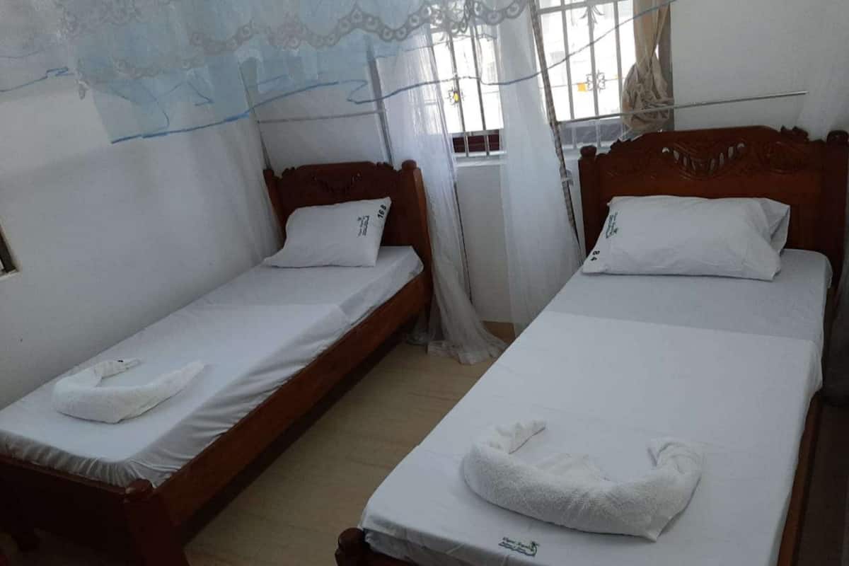Two single beds with white linens and towels, a wooden headboard, and a window with a curtain.