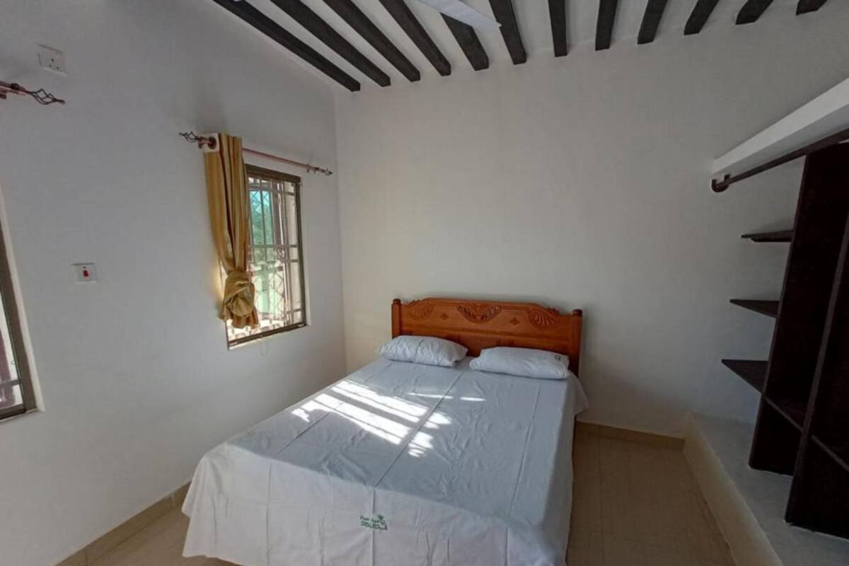 A bedroom with a bed, a window with curtains, and a ceiling with wooden beams.