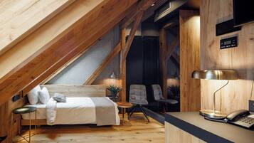 Un dormitorio estilo loft con techo inclinado, una cama, un escritorio, dos sillas y una mesita.