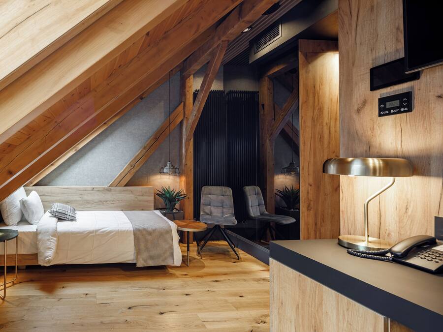 Un dormitorio estilo loft con techo inclinado, una cama, un escritorio, dos sillas y una mesita.