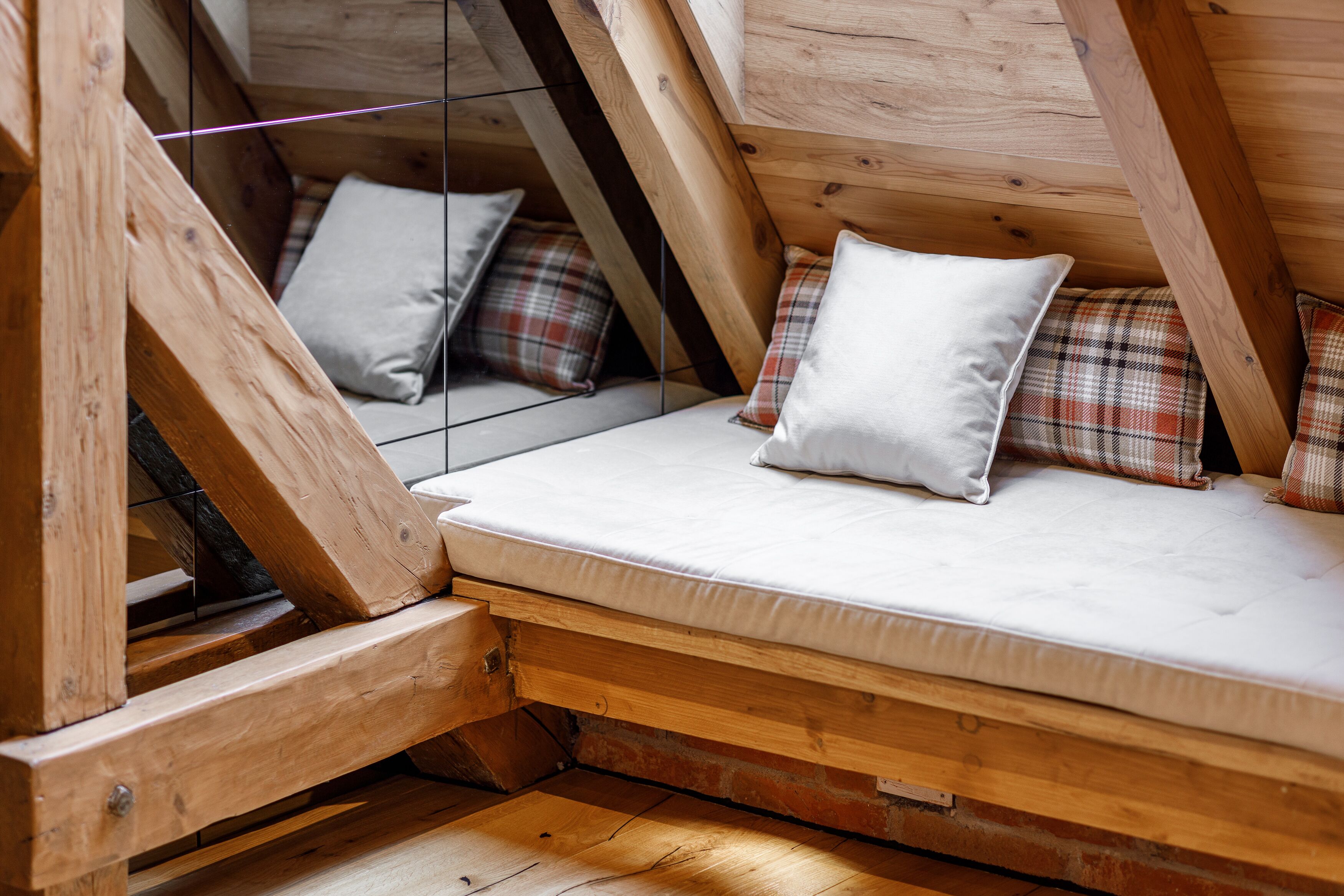 A loft-style bedroom with a wooden sloped ceiling, a mattress with pillows, and a brick wall.