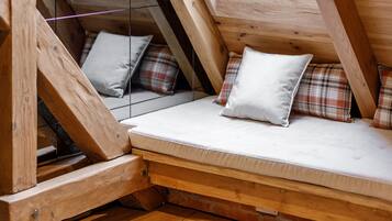 A loft-style bedroom with a wooden sloped ceiling, a mattress with pillows, and a brick wall.
