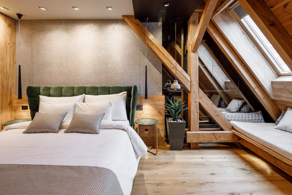 A bedroom with a lofted sleeping area, wooden beams, and a large window.