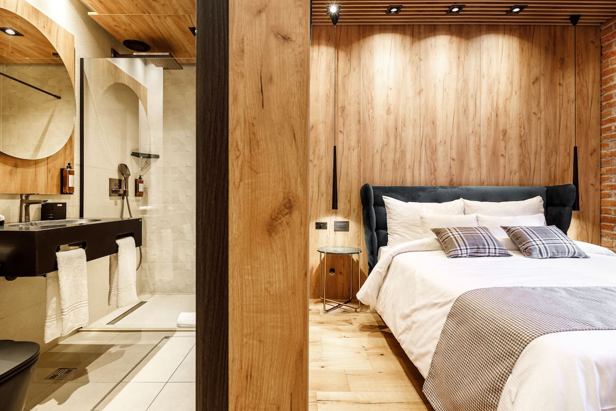 A modern bedroom with a wooden ceiling, a large bed with white bedding, and a small bedside table.