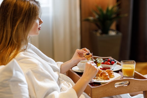 A person in a white robe sitting at a wooden table with breakfast items including croissants, fruit, and orange juice. - Schuster Boarding House (Brasov)