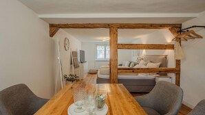 A wooden dining table with chairs, a wooden ceiling beam, a bed with pillows, a TV, and a window. - Time out in the historic half-timbered house in Bad Buchau  (Bad Buchau)