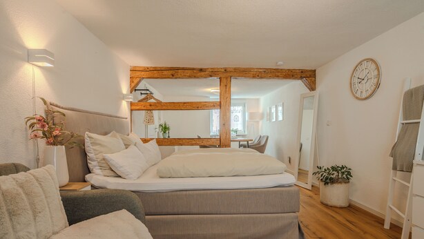 A bedroom with a bed, a sofa, a wooden floor, a wall clock, and a mirror. - Time out in the historic half-timbered house in Bad Buchau  (Bad Buchau)