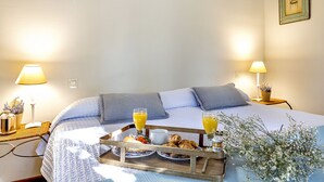 Una cama bien hecha con una bandeja de desayuno, que incluye croissants y zumo de naranja, en una habitación con dos lámparas de noche y un cuadro en la pared.