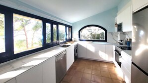 Una cocina con armarios blancos, lavavajillas, un fregadero y una ventana con vista a árboles.
